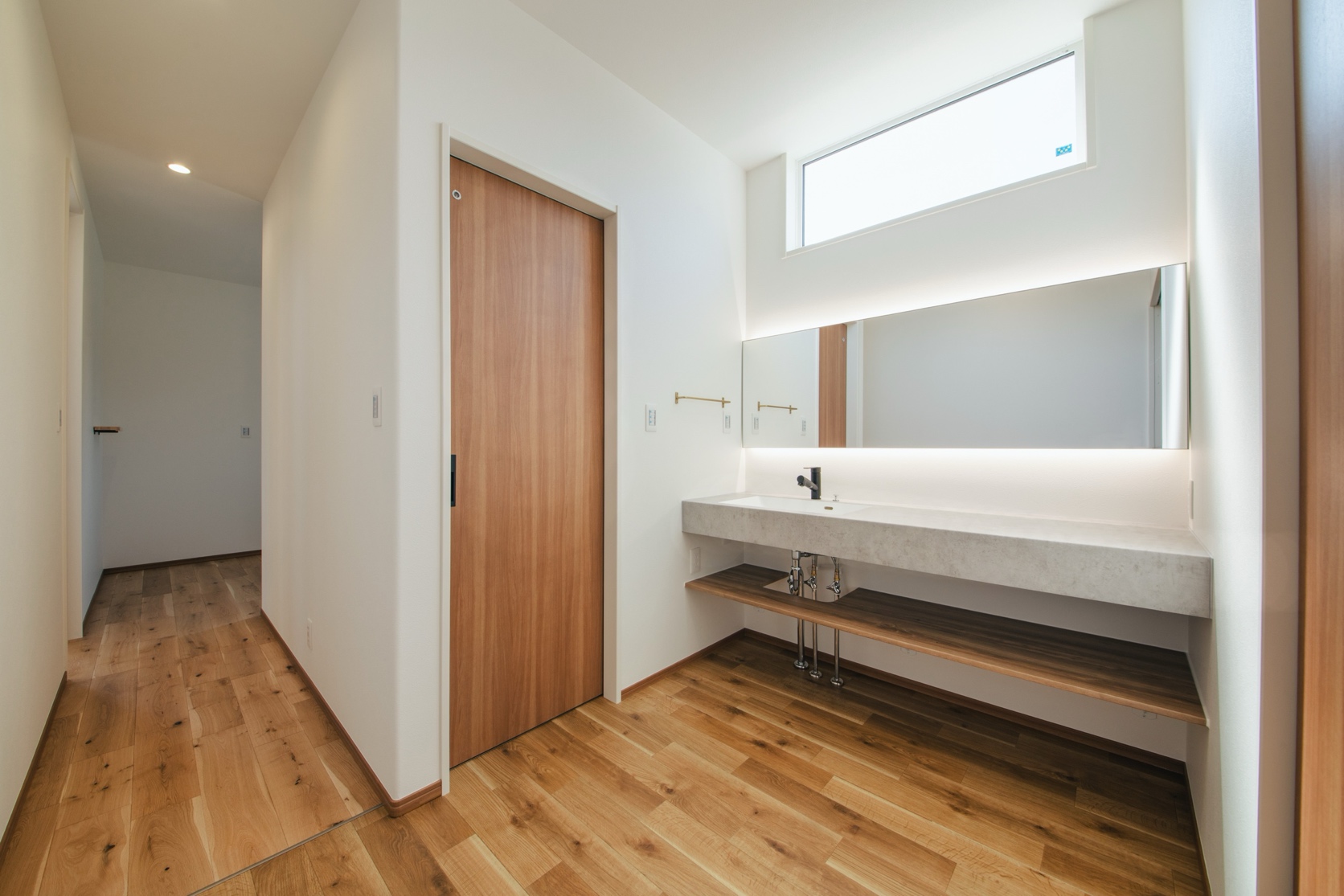 玄関からさらに室内へと足を進めると、トイレに隣接した洗面コーナーが。ミラタップの鏡の後ろに間接照明を取り入れた洗面スペースは、幅広カウンターで使いやすく。